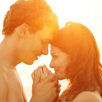 A young loving couple hugging and kissing on the beach at suns